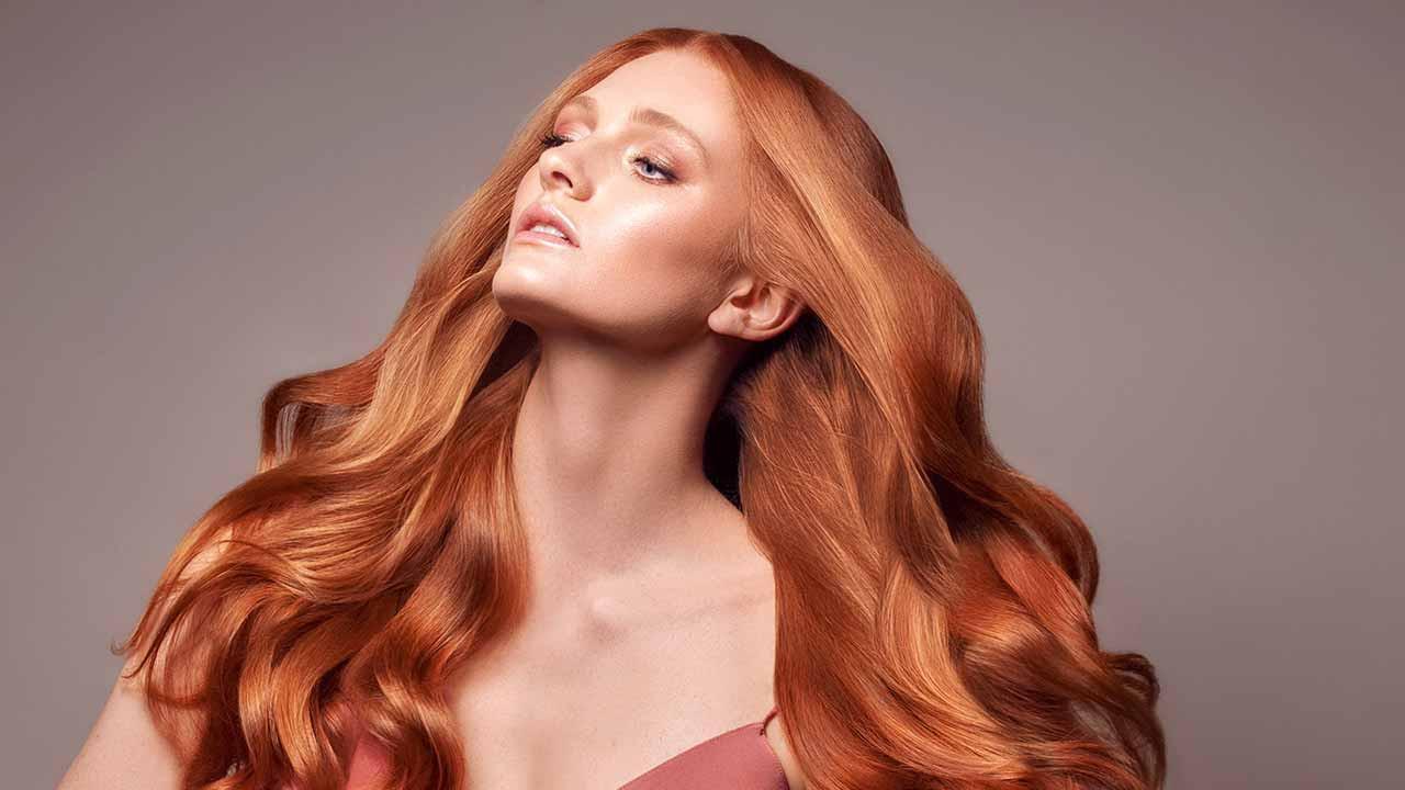 A person with long, flowing red hair poses confidently against a neutral background.