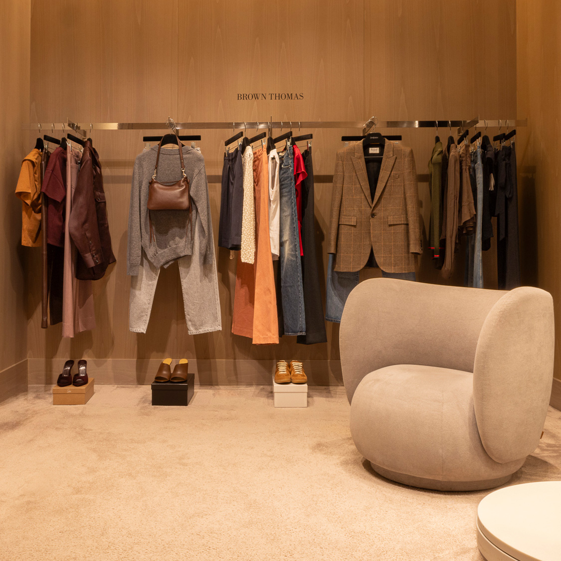 Chic clothing store fitting room with racks, modern chairs, and full-length mirror.